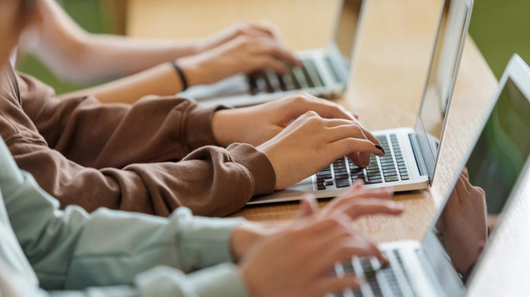 Three young individuals sitting down in a row, typing on laptops