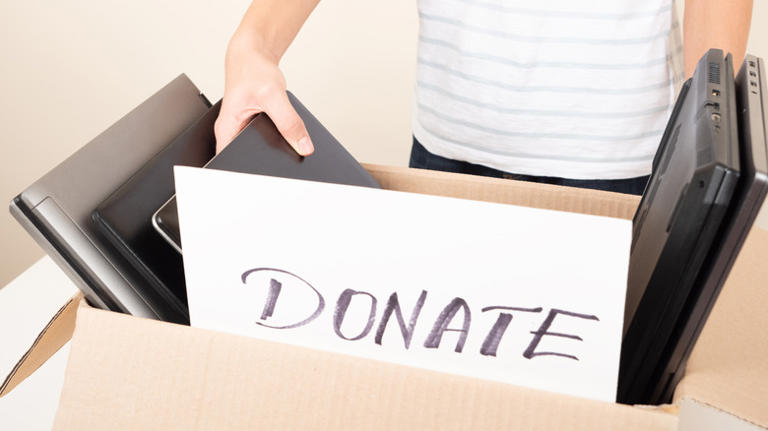 A person standing behind a box of laptops, with the the front of the box having a card that has the word donate written on it