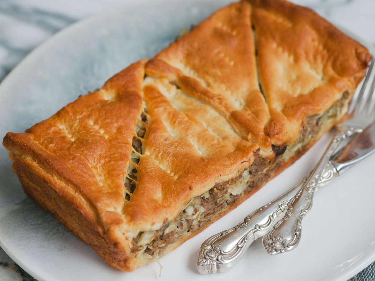 close up view of a Runza Casserole pastry with ground beef and onions on a plate with a fork and knife