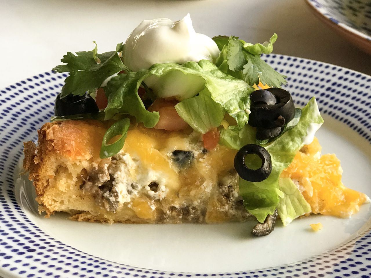 close up view of Crescent Taco Pie garnished with lettuce, black olives and sour cream on a plate