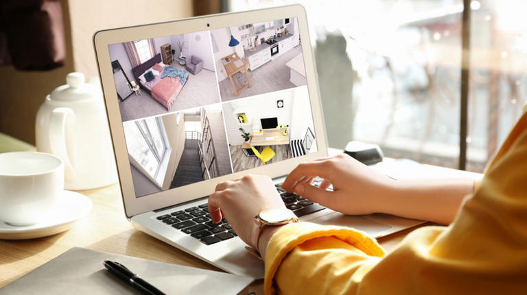 A pair of hands on a laptop keyboard as display shows security footage of multiple rooms in a house