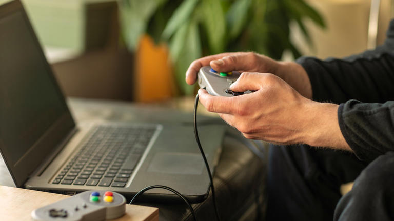 A pair of hands holding an SNES controller in front of a laptop
