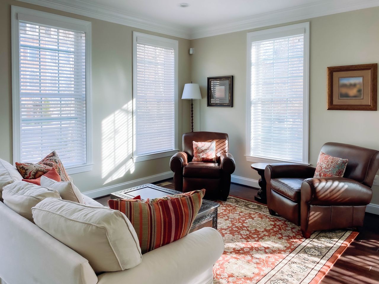 A cozy living room with upholstered chairs a white sofa large windows and framed artwork on the walls