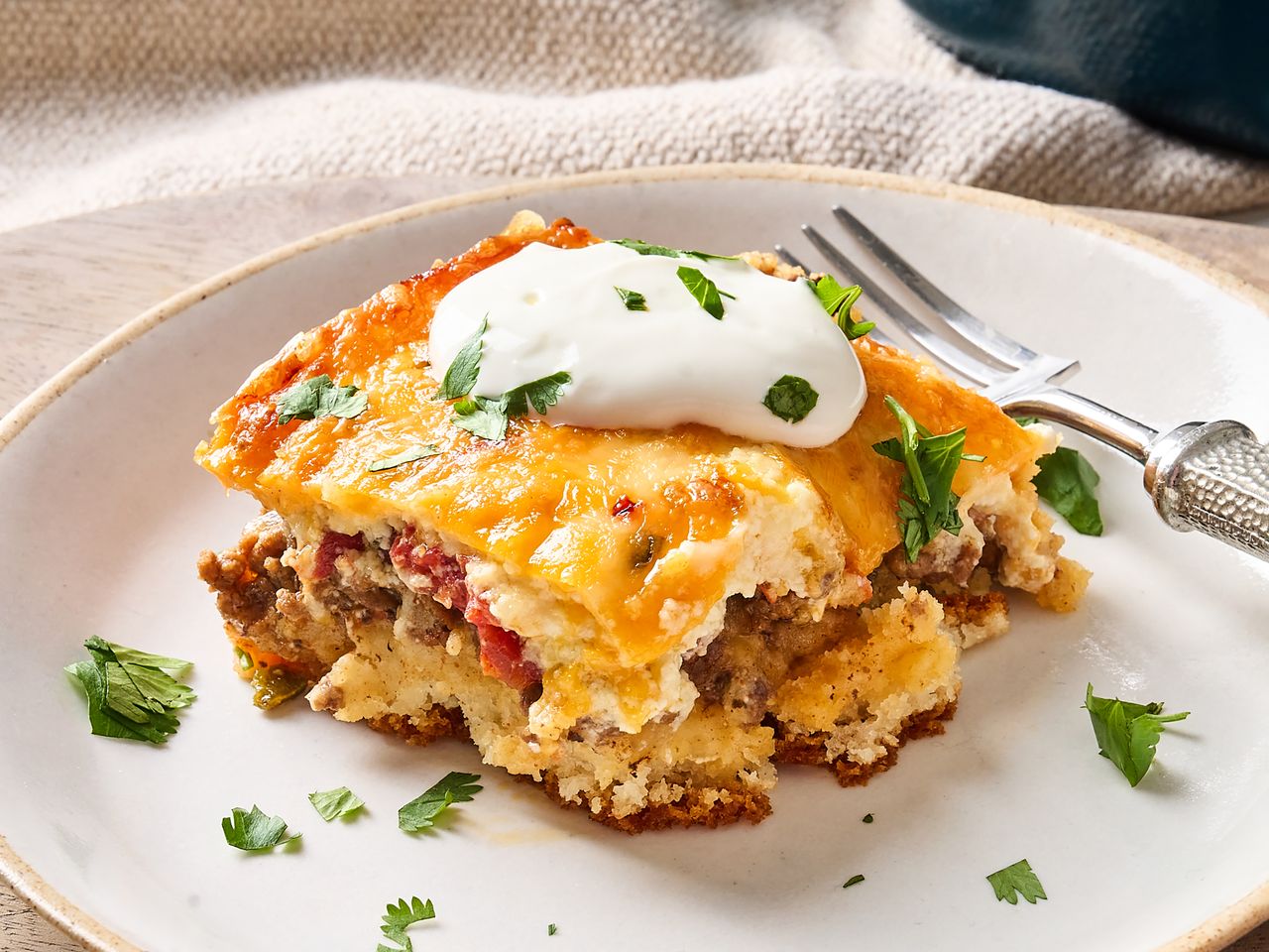 A serving of casserole on a plate topped with sour cream and garnished with herbs fork nearby