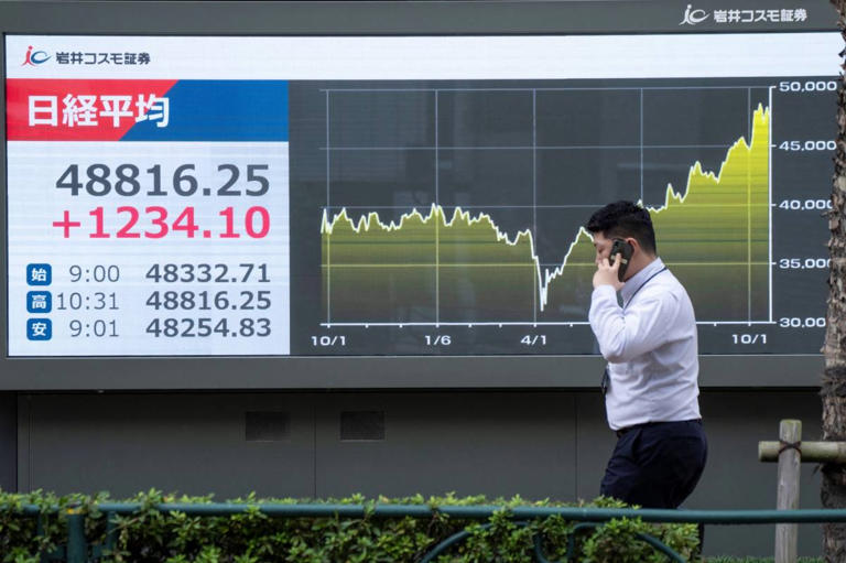A man walks past an electronic quotation board displaying numbers of the Nikkei Stock Average on the Tokyo Stock Exchange in Tokyo on October 20, 2025. (Photo by Kazuhiro NOGI / AFP)