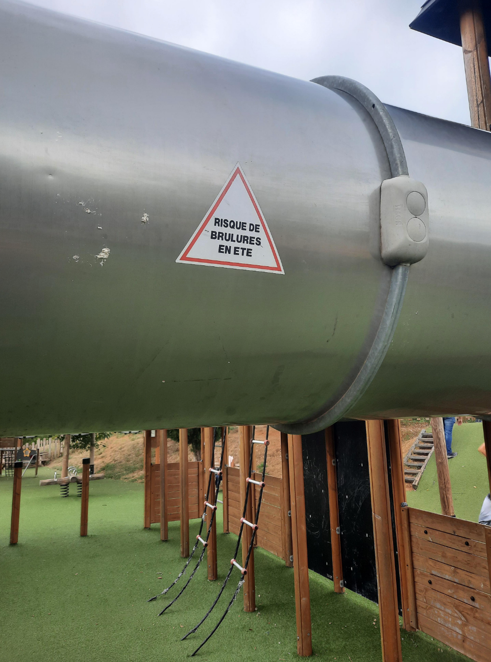 Warning sign on a metal slide about burn risk in summer, written in French