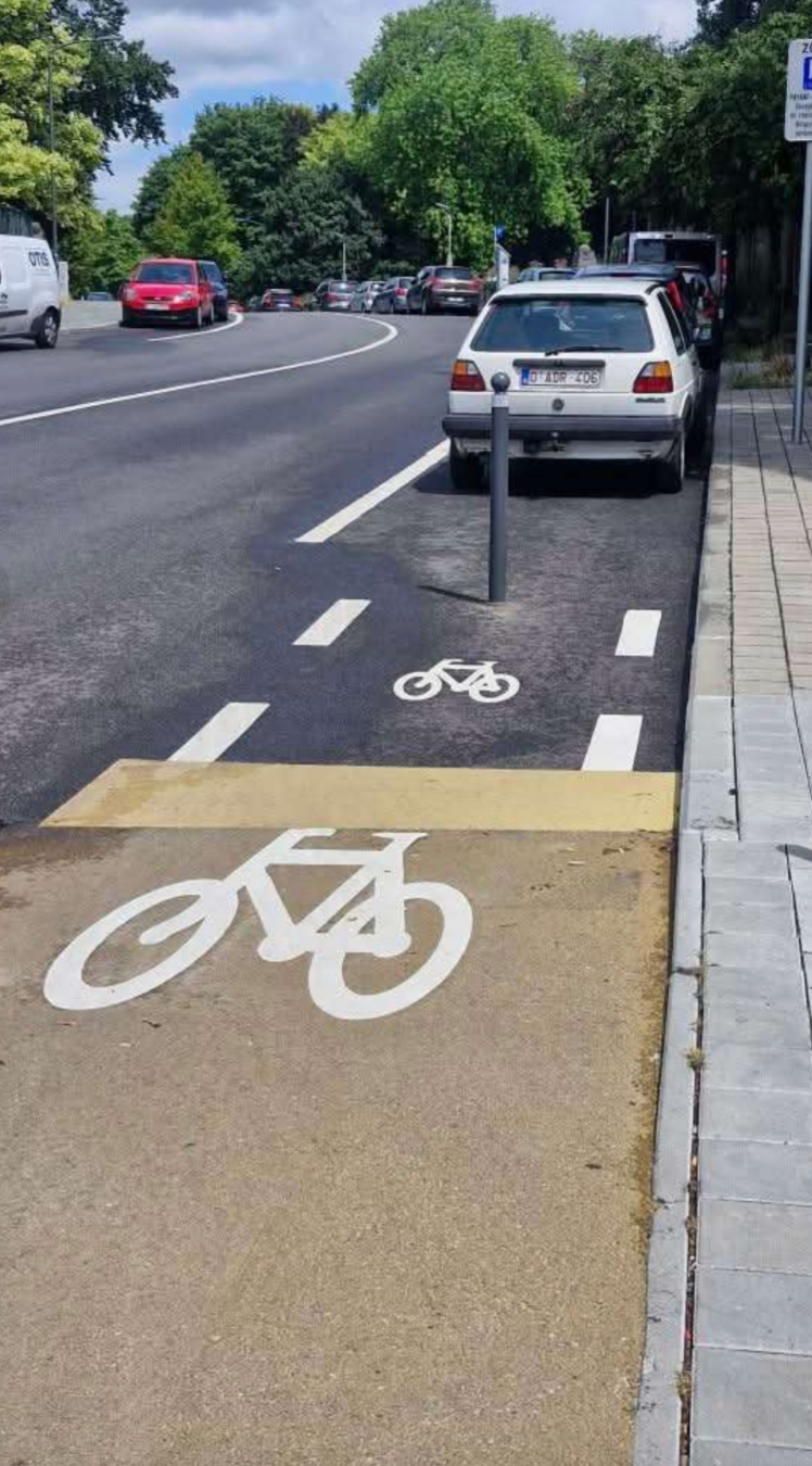 Bike lane on a street is blocked by a parked car, with bike symbols painted on both pavement and road