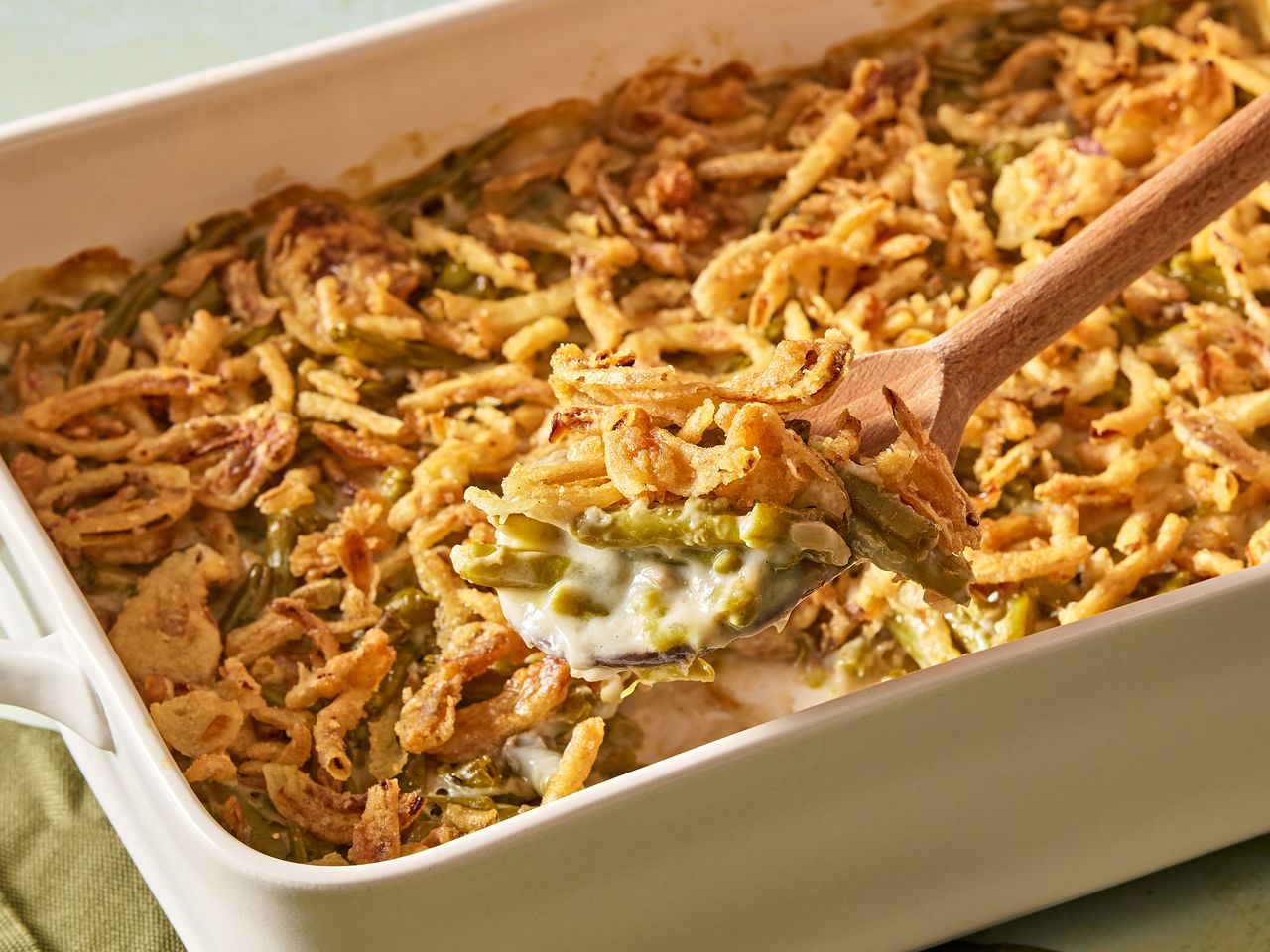 A spoon removing a portion from a green bean casserole topped with crunchy fried onions