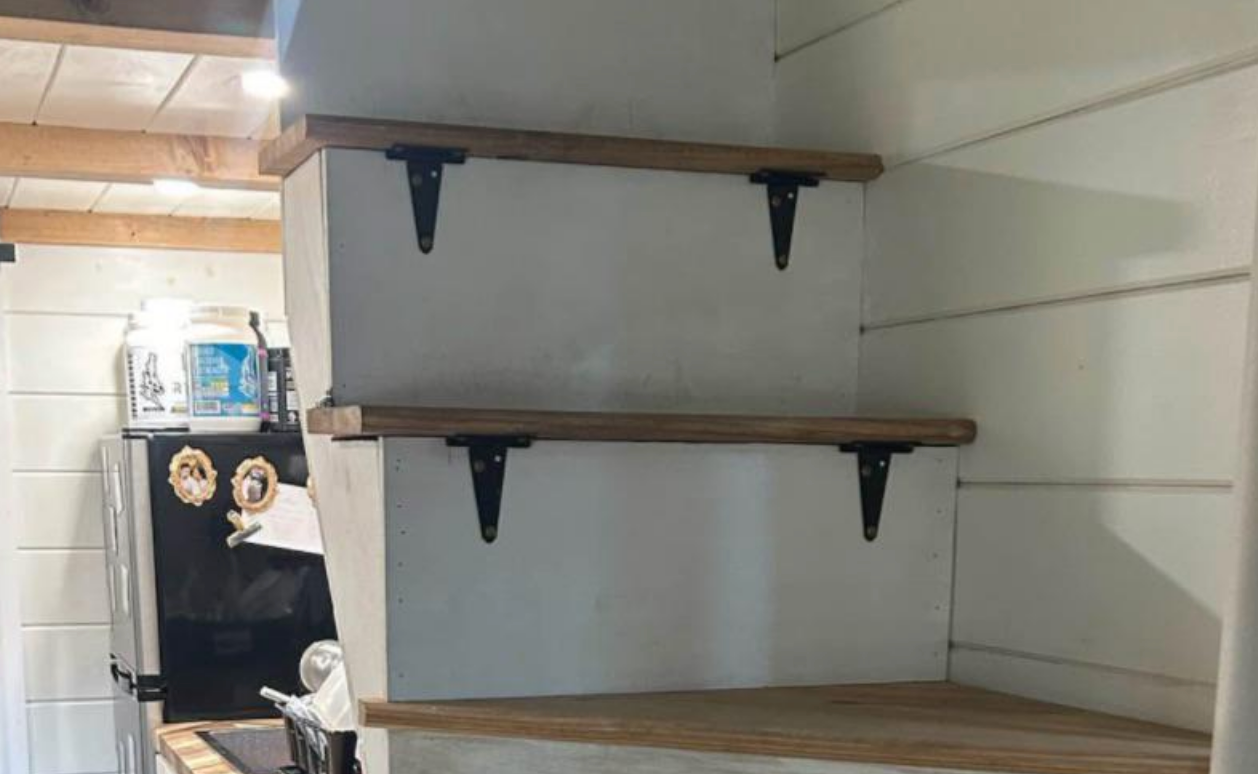 Compact staircase integrated into a small living space with wooden treads and metal brackets, adjacent to a visible kitchen area