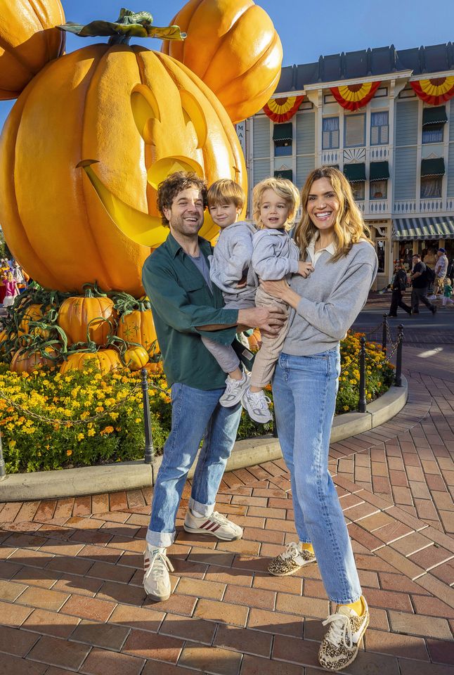Mandy Moore, Taylor Goldsmith, and sons Gus and Ozzie posing in front of a large decorative pumpkin with Mickey Mouse ears at Disneyland during Halloween