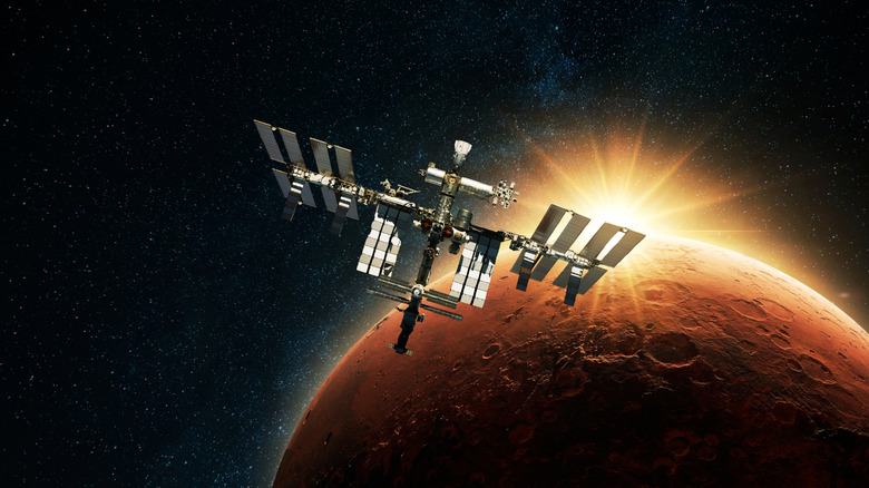 A space station floating in the orbit of Mars with the sun glaring in behind it.