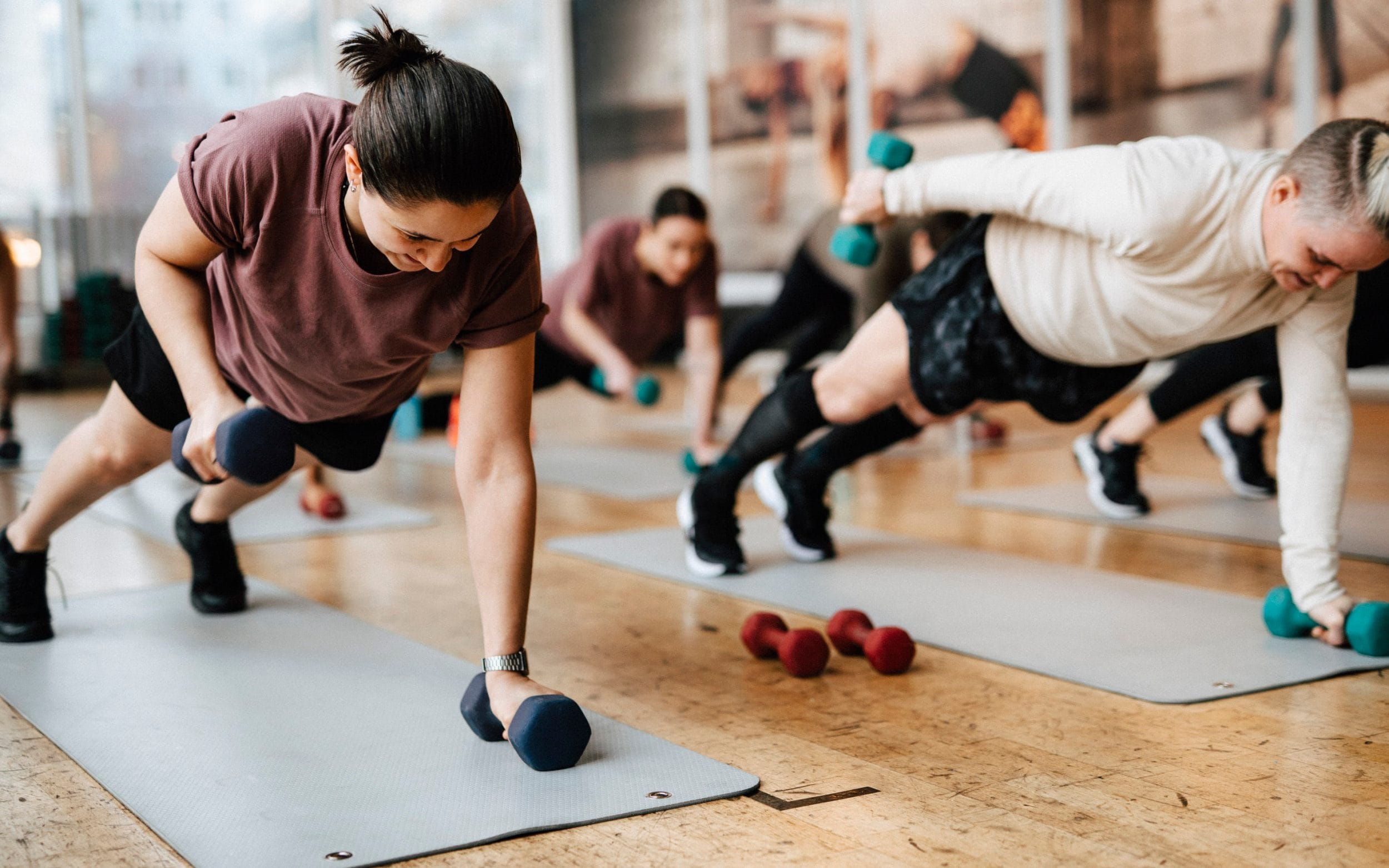 Group of people exercising with dumbbells on mats at a gym