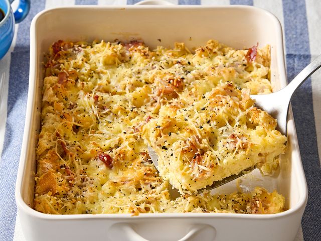 A casserole dish containing a cooked breakfast casserole with a serving being lifted by a spatula