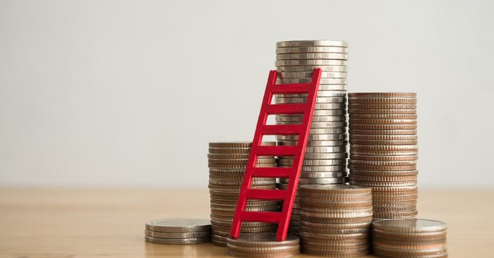 Stacks of coins in varying heights with a ladder leaning against the tallest one.