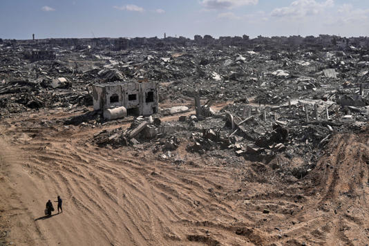 Two displaced Palestinians walk past destroyed buildings in the heavily damaged Sheikh Radwan neighborhood in Gaza City (AP Photo/Abdel Kareem Hana)