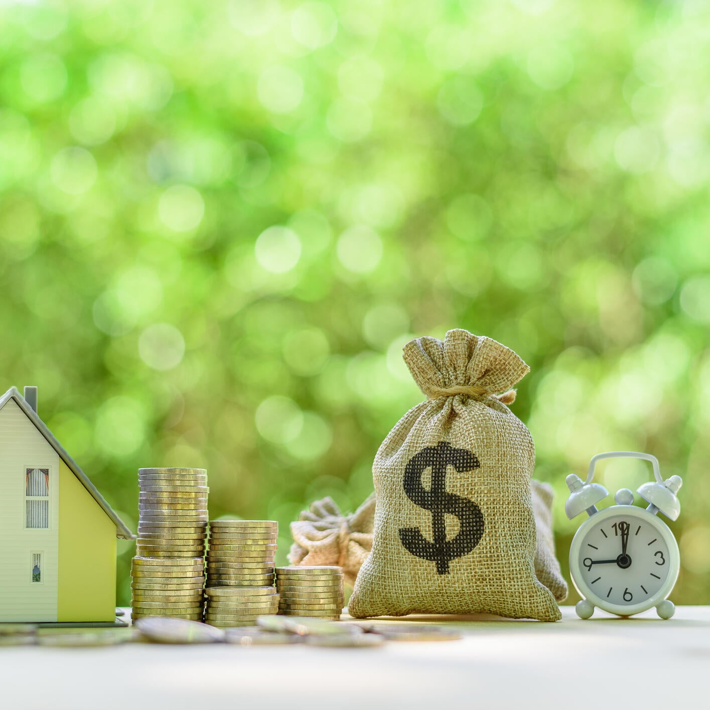 Mortgage-backed security MBS, financial concept : House model, stacks of rising coins, US dollar, money bags, a clock on a table over green background, depicts investment in home bought from the bank