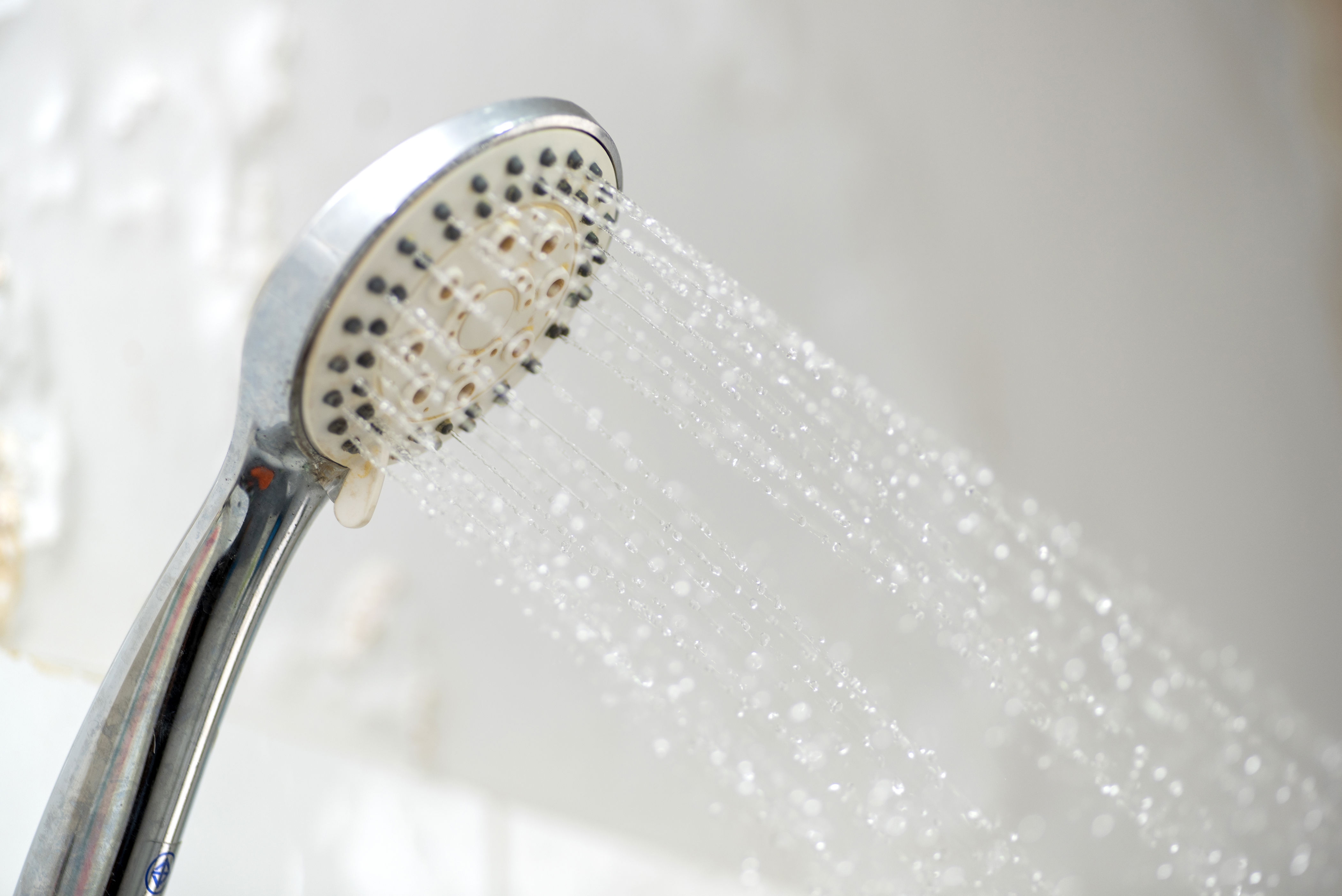 Close-up of a showerhead spraying water, angled to the right, with droplets visible mid-air