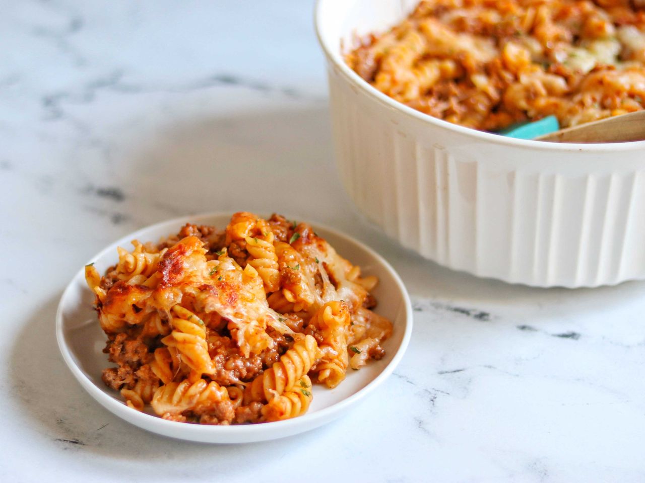 pasta casserole with fussili, ground beef, and cheese on white plate with casserole in the background