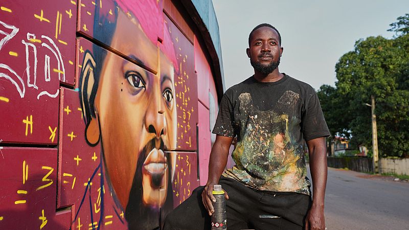 Le graffeur Omar Diaw pose à côté de sa fresque représentant le président guinéen Mamadi Doumbouya 20 septembre 2025. (AP Photo/Misper Apawu)