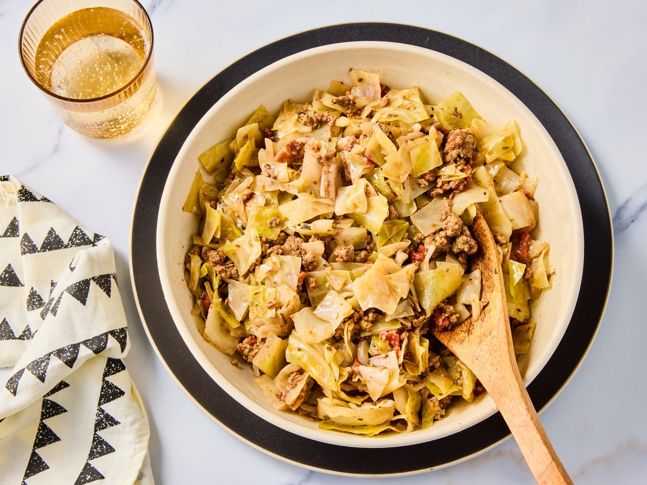 A large bowl of ground beef and cabbage with a wooden serving spoon, served with a glass of sparkling water