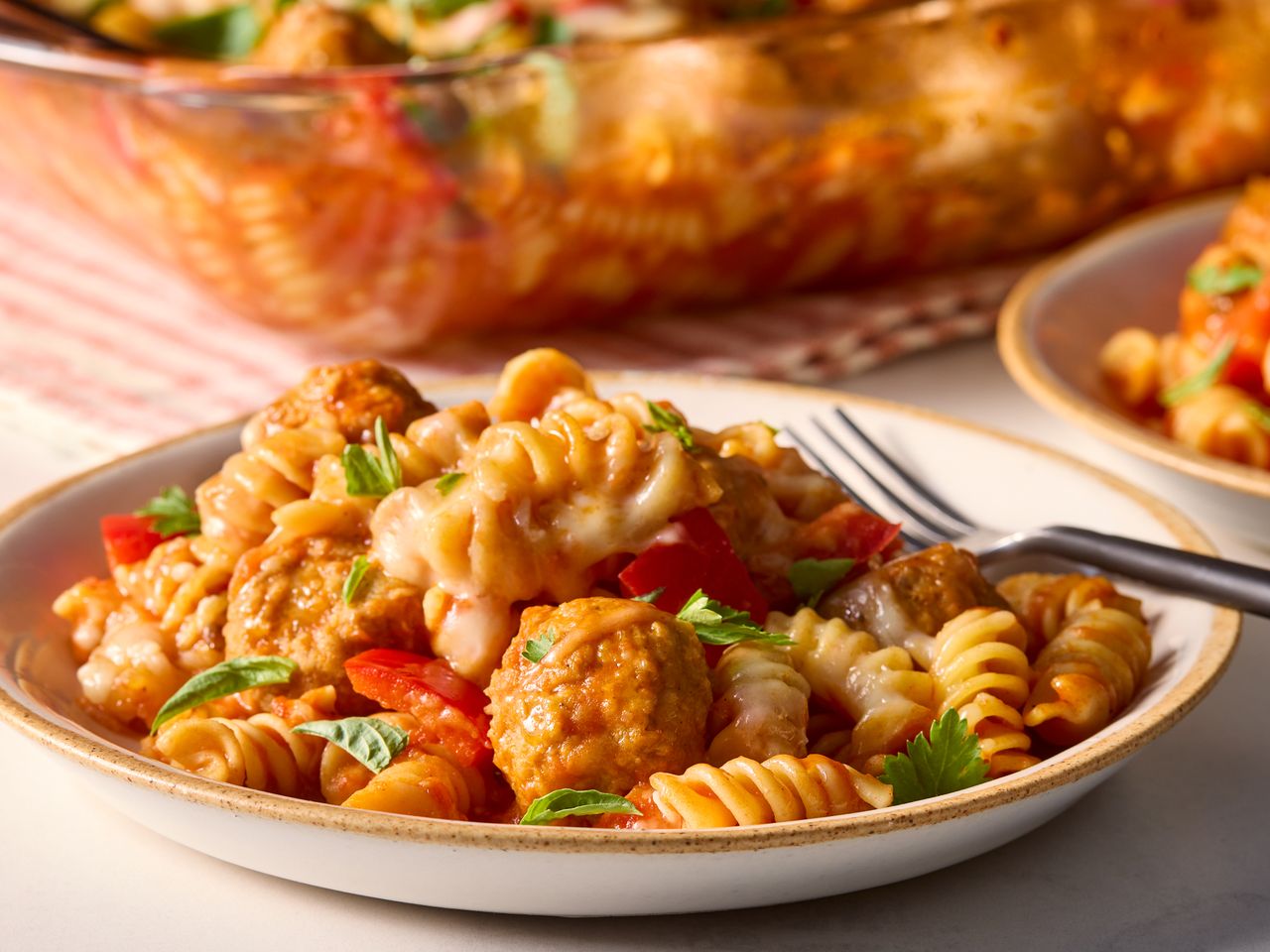 A plated serving of Dump and Bake Meatball Casserole garnished with fresh herbs, with a fork on the side