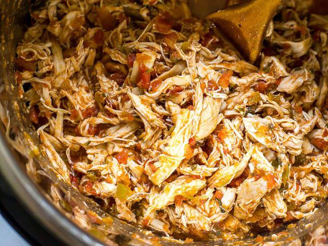 top-down view of shredded chicken with salsa in a pot with a wooden spoon