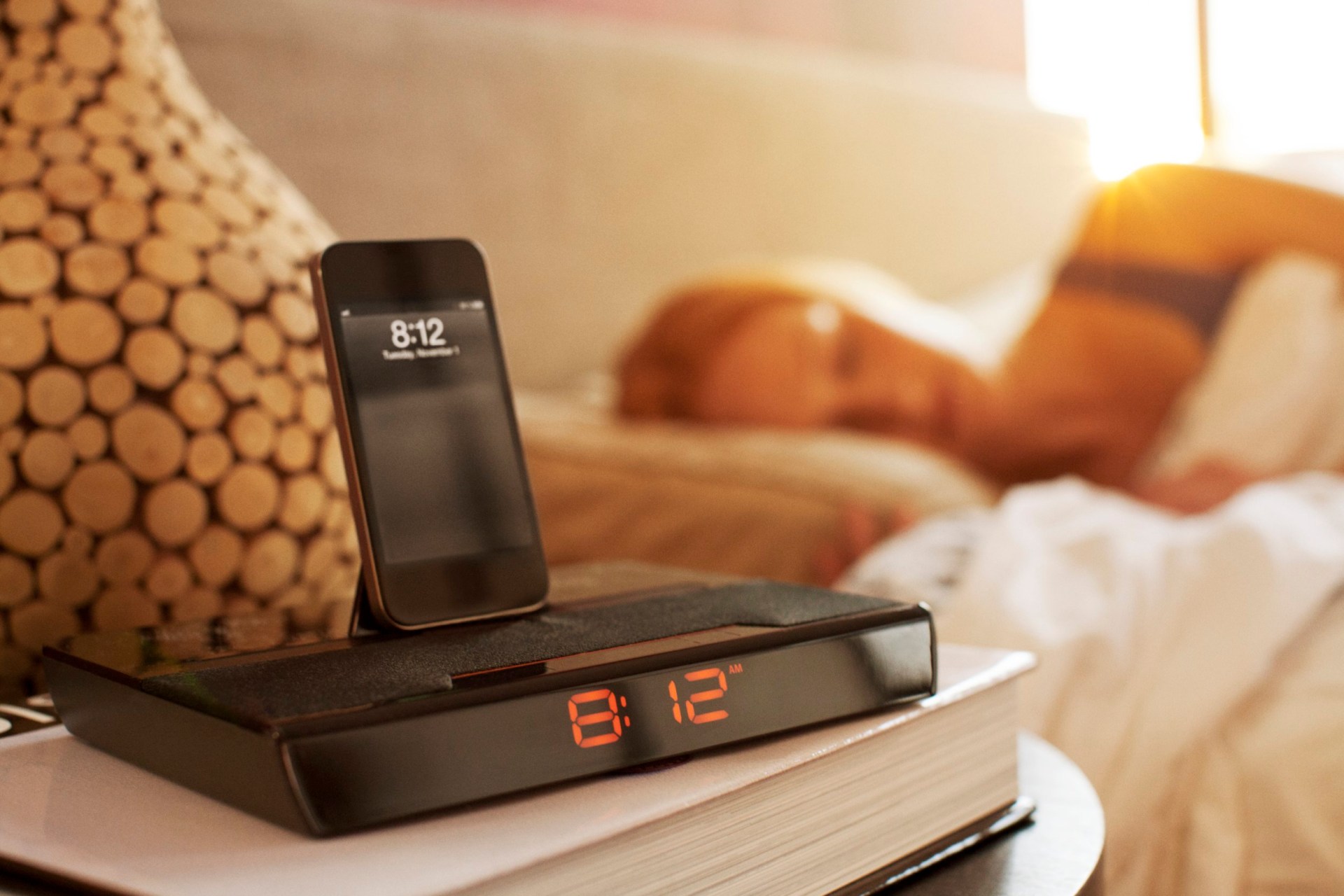 An iPhone is seen resting on top of an alarm clock as a woman sleeps nearby