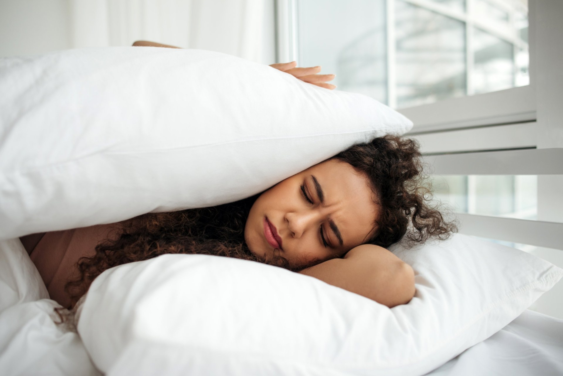 A woman lies on the bed and covered herself with pillows