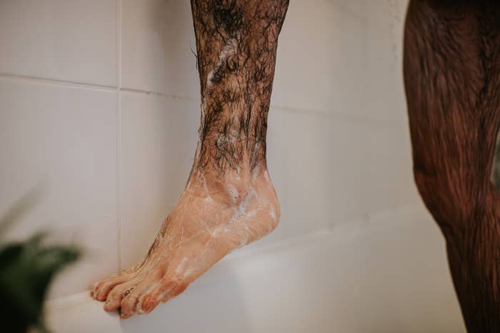 Foot covered in shaving cream balanced on the edge of a bathtub, ready for shaving