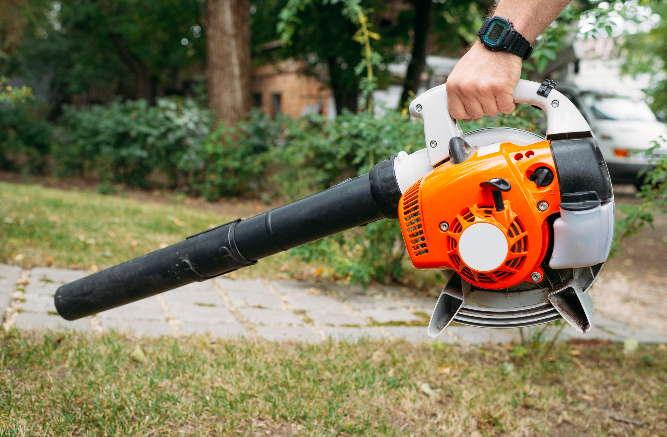 A person holds a handheld leaf blower outdoors, ready for use on a grassy area