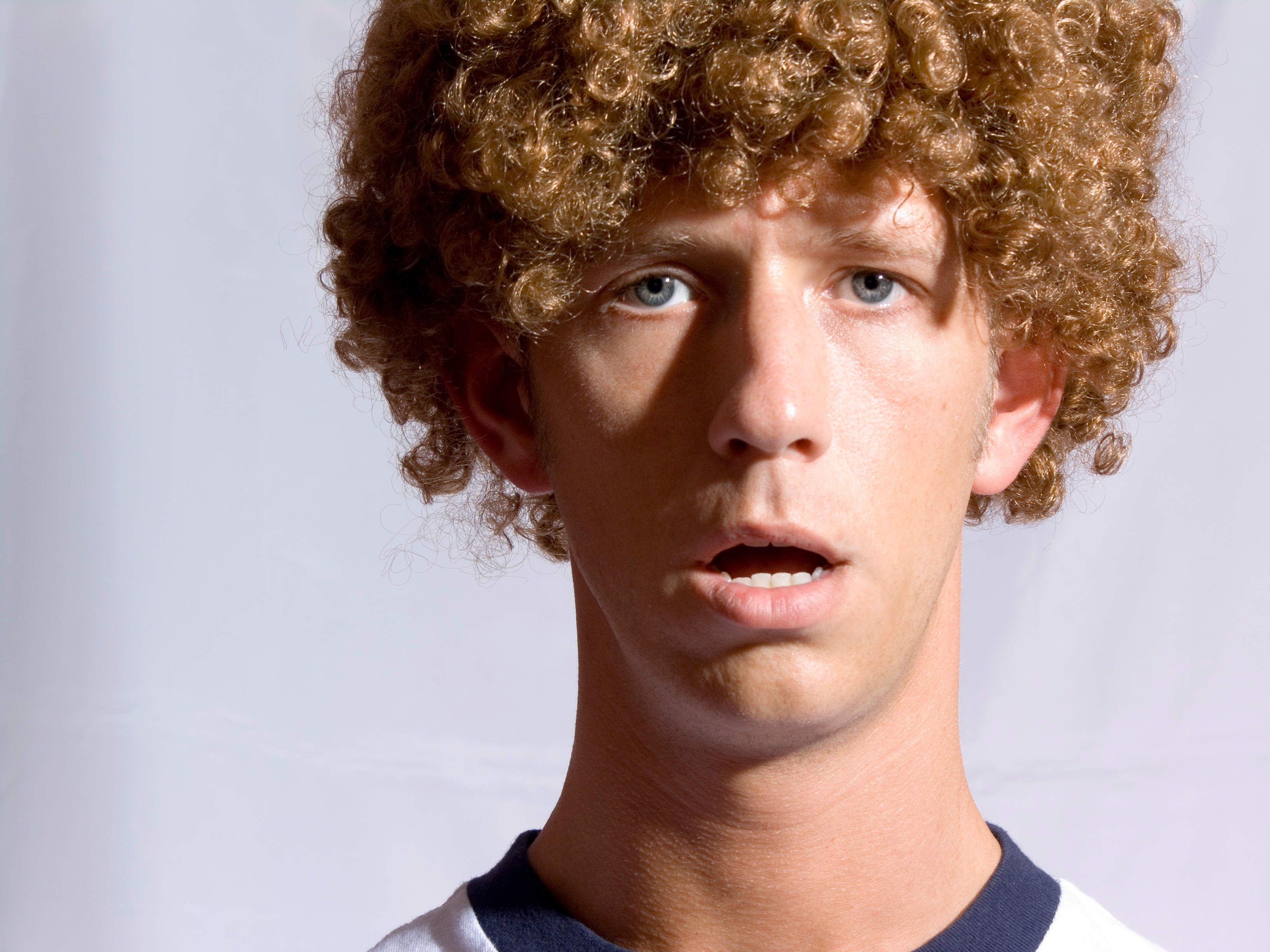 Person with curly hair looking surprised against a plain background