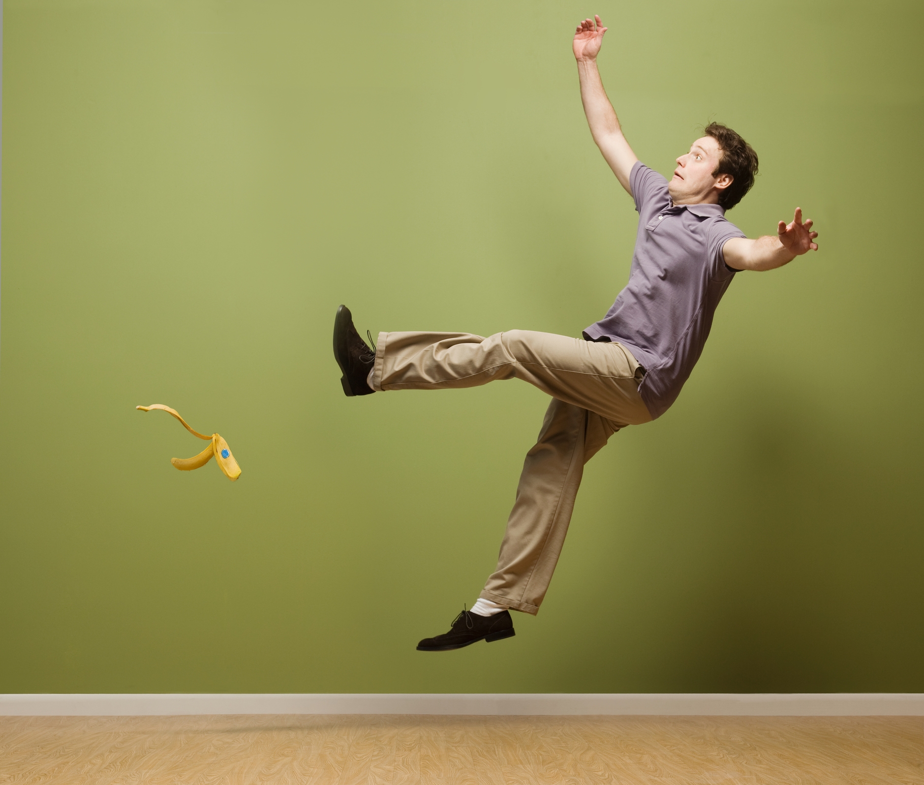 Person slipping on a banana peel in a comical pose, wearing a casual shirt and pants, with arms and legs flailing in the air