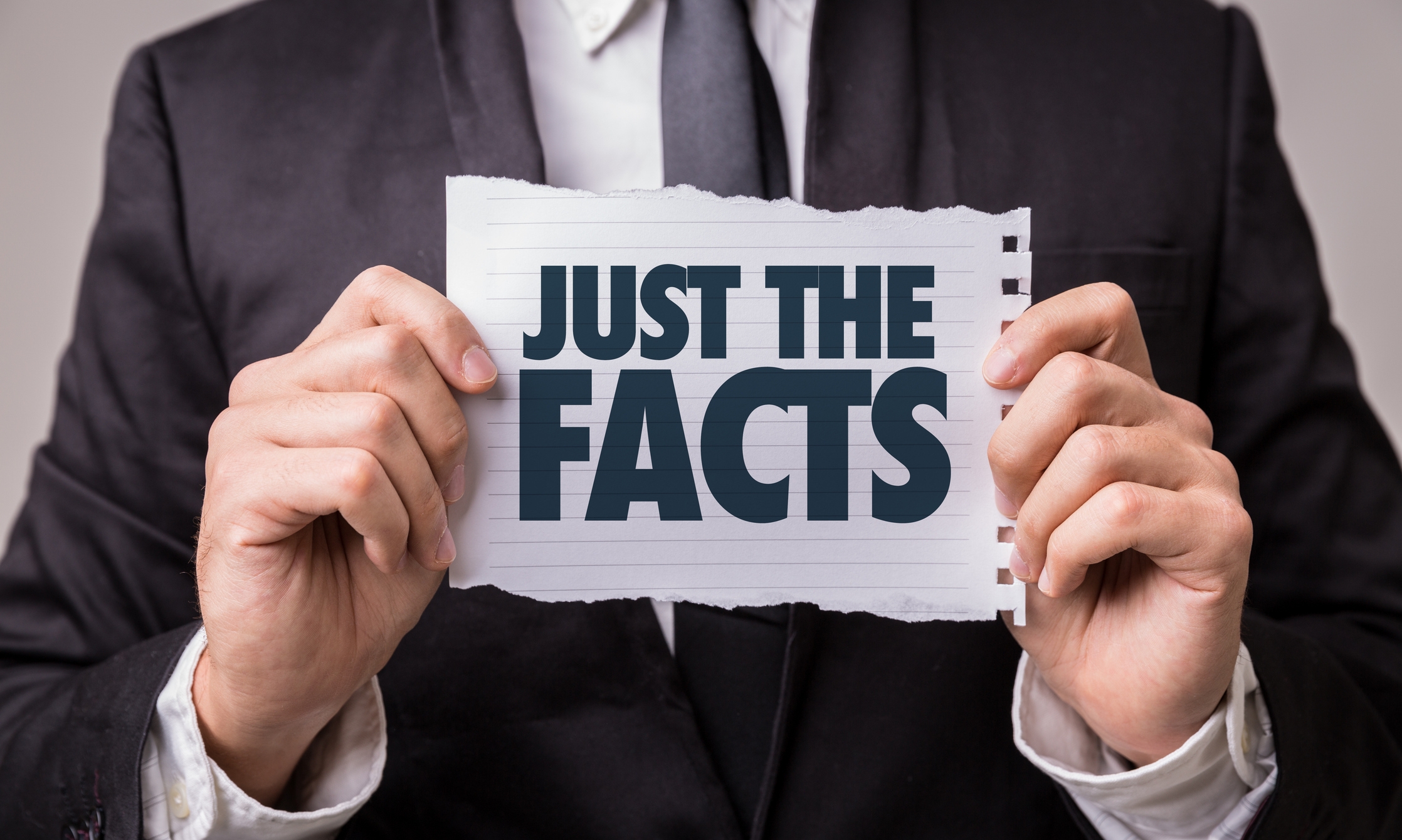 Person holding a paper with the text "JUST THE FACTS" in capital letters