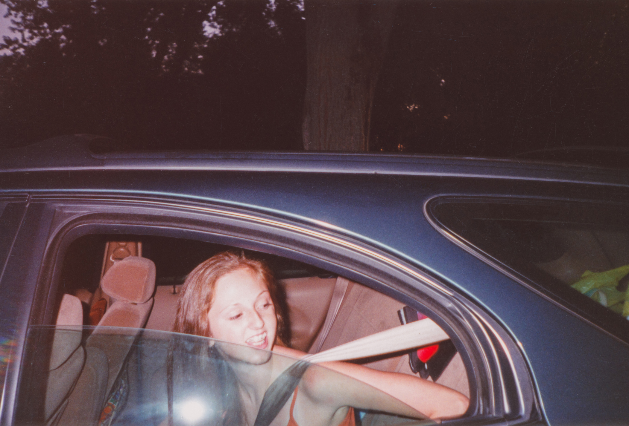 Person smiling and sitting in a car, looking outside the open window