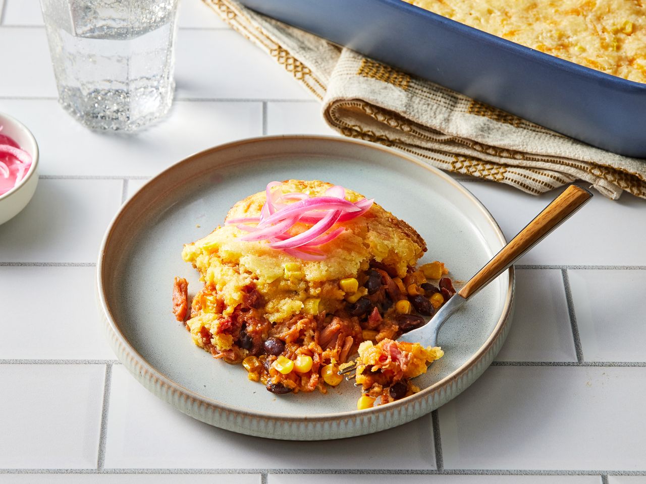 Pulled Pork Casserole garnished with pickled red onions on a plate with a fork, with a baking dish in the background
