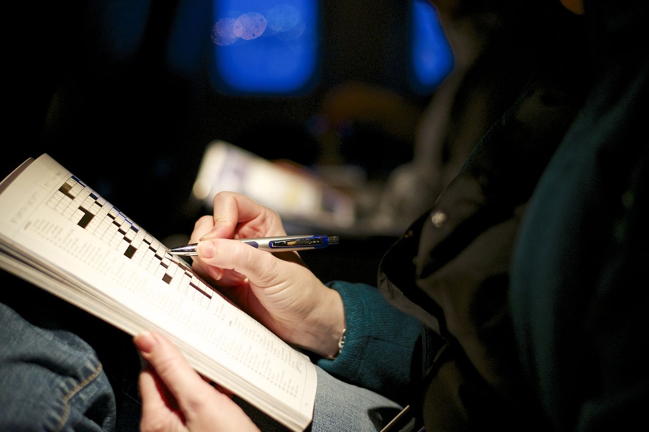 Woman's hands, playing crossword puzzle on plane at dawn