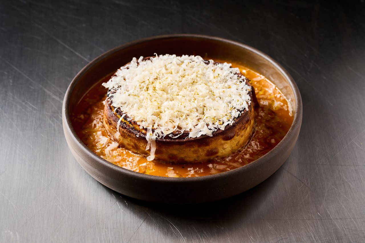 A dish featuring a flanlike item topped with grated cheese in a brown liquid sauce