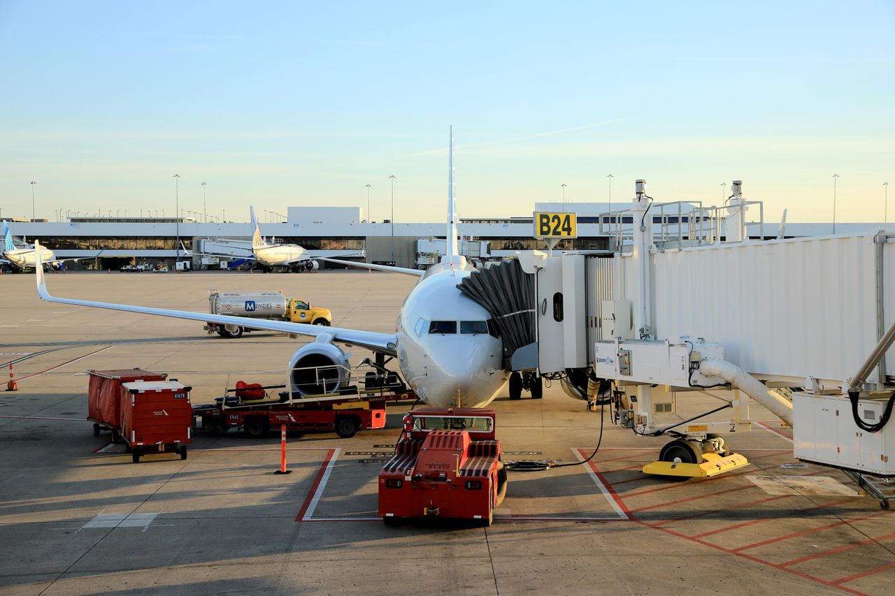 An airplane docked at a jet bridge at an airport gate ground support vehicles and equipment nearby