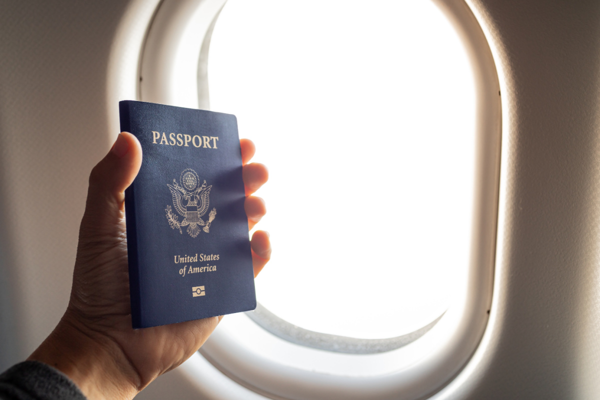 Passenger holding a USA passport in a plane with the window in the background