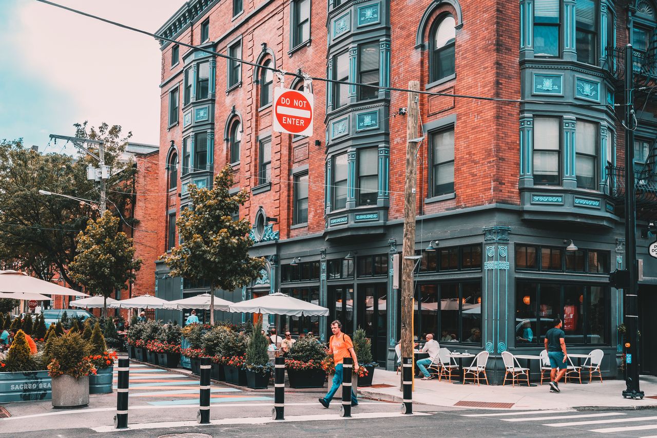 A busy street corner featuring a redbrick building with outdoor seating and decorations on the sidewalk