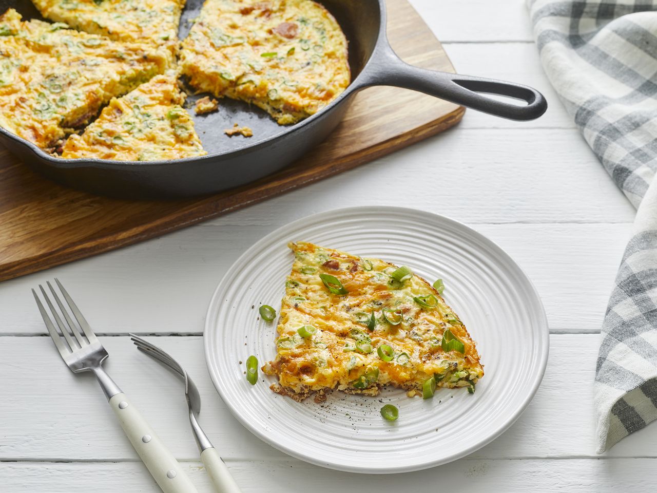 looking at a single slice of bacon cheese frittata on a plate with the remaining in a cast iron skillet behind