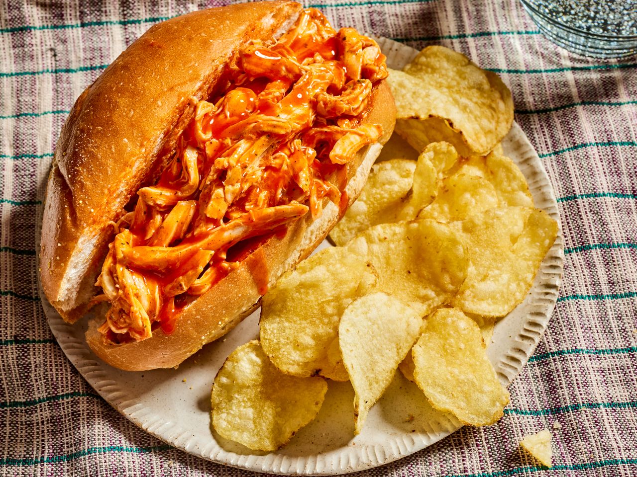 Pulled buffalo chicken sandwich served with potato chips on a plate