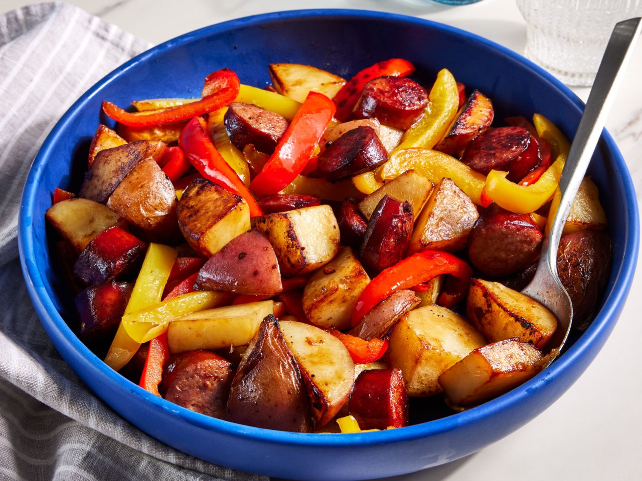 Kielbasa with peppers and potatoes served in a blue bowl.