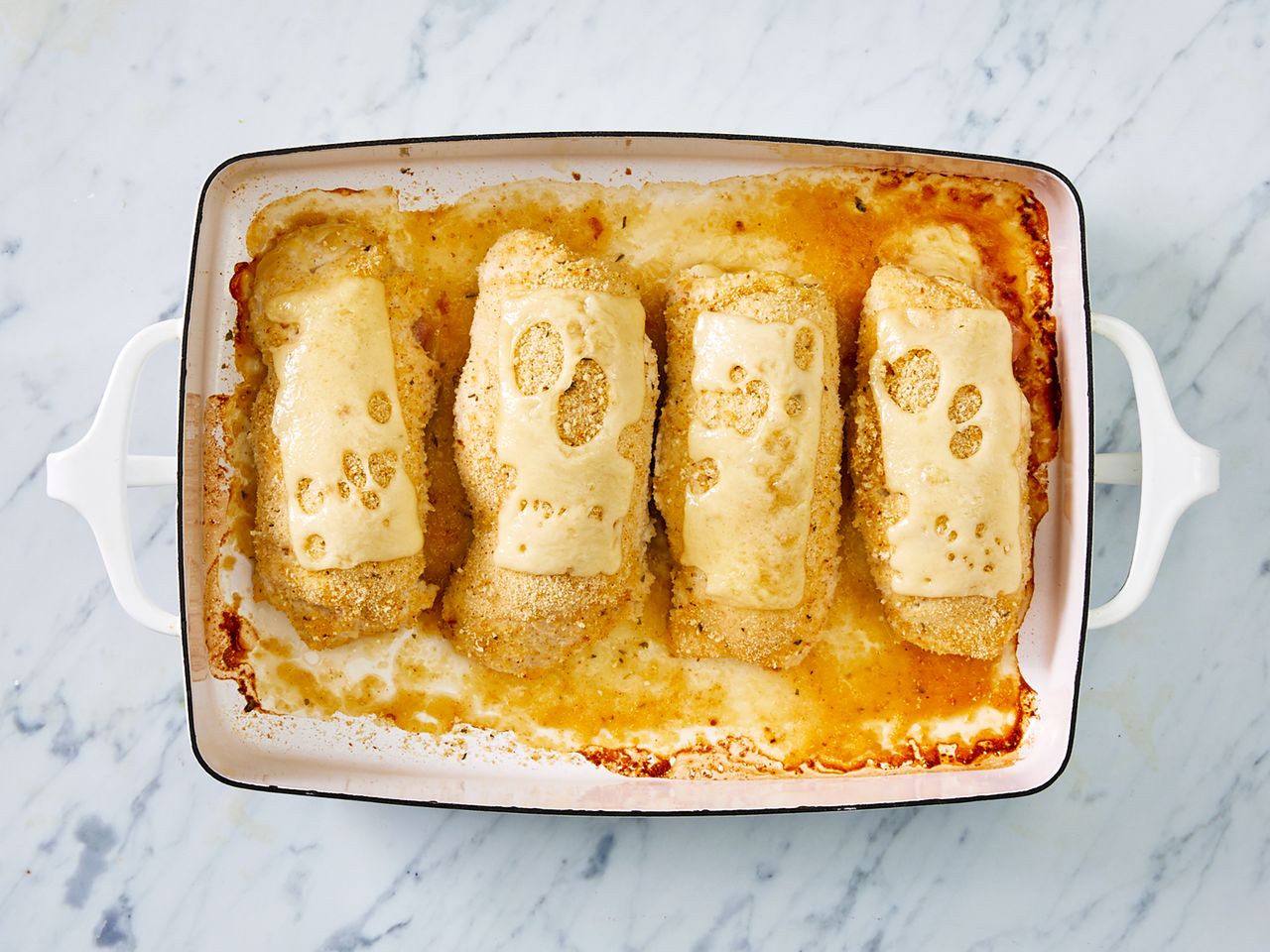 a top down view of 4 golden-brown chicken cordon blues in a baking dish, each topped with melted Swiss cheese