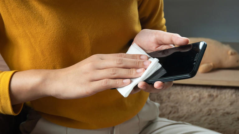 A woman cleaning a phone screen with a cloth.