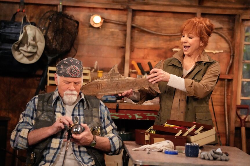 Emmett (Rex Linn) polishes a fishing pole as&nbsp;Bobbie (Reba McEntire) holds a wooden fish to his place on Happy's Place Episode 104.