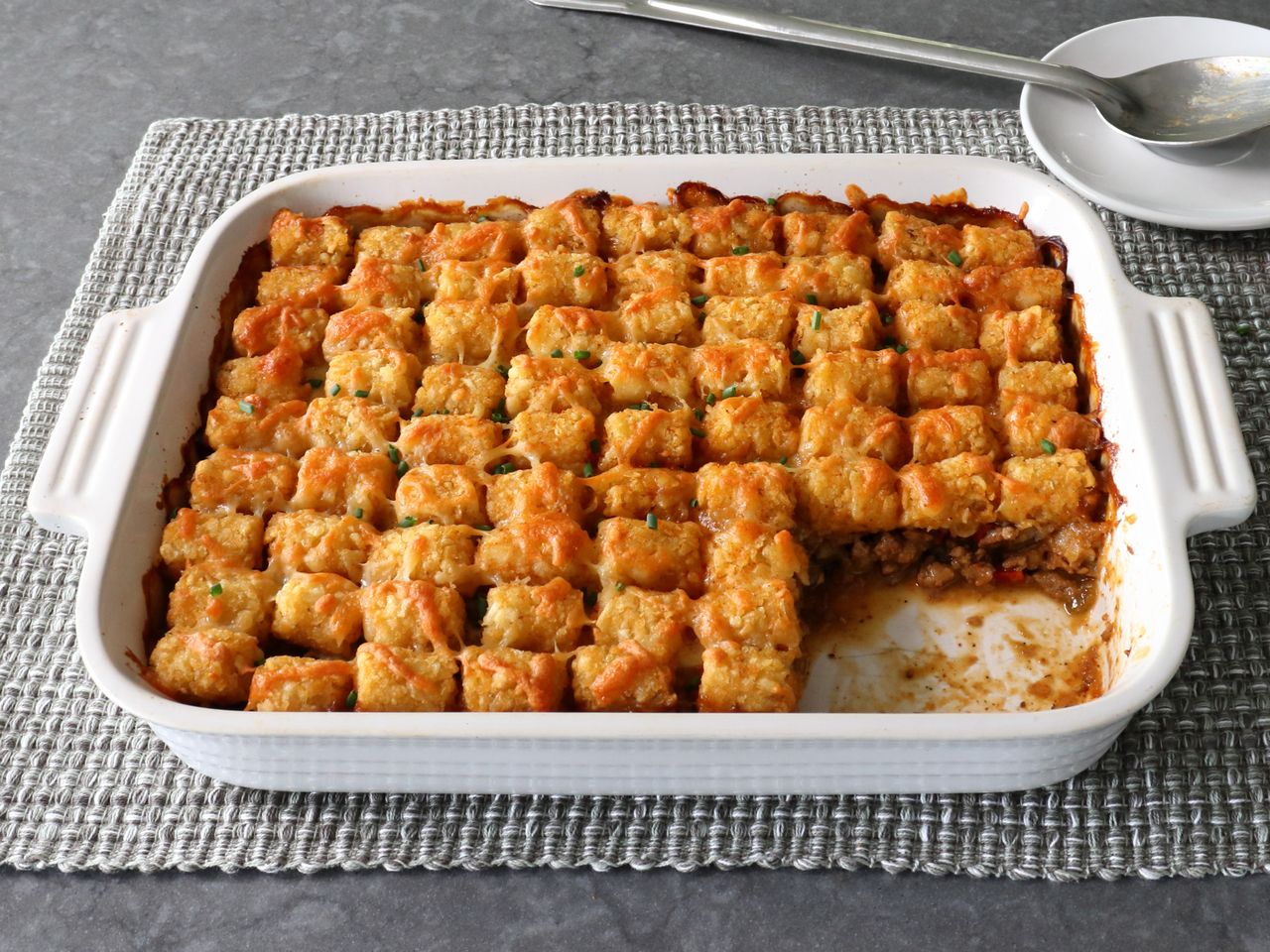 beautifully golden tater tot hot dish in white casserole dish on gray placemat