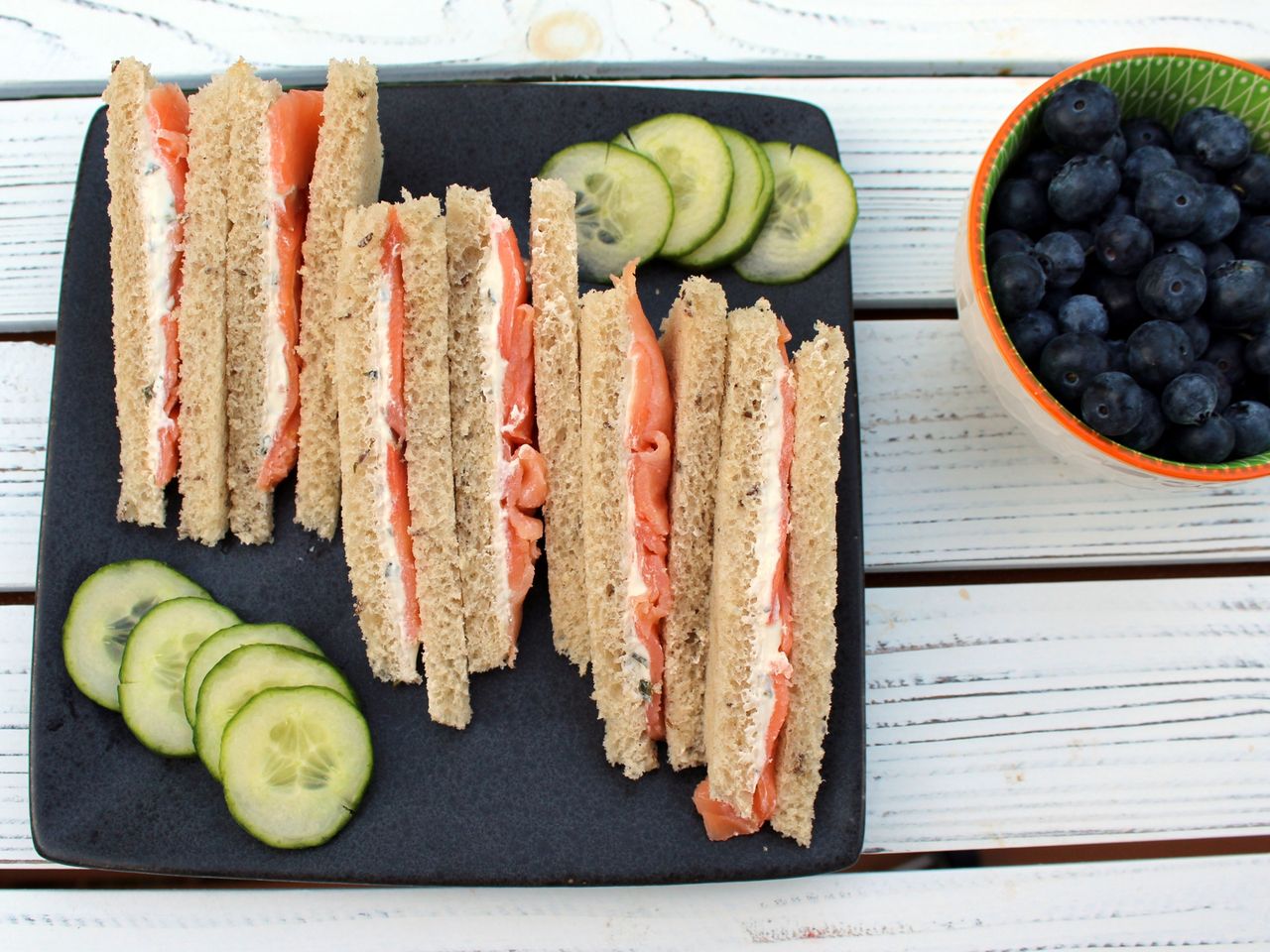Salmon and chive sandwiches with sliced cucumbers and some blueberries in the corder