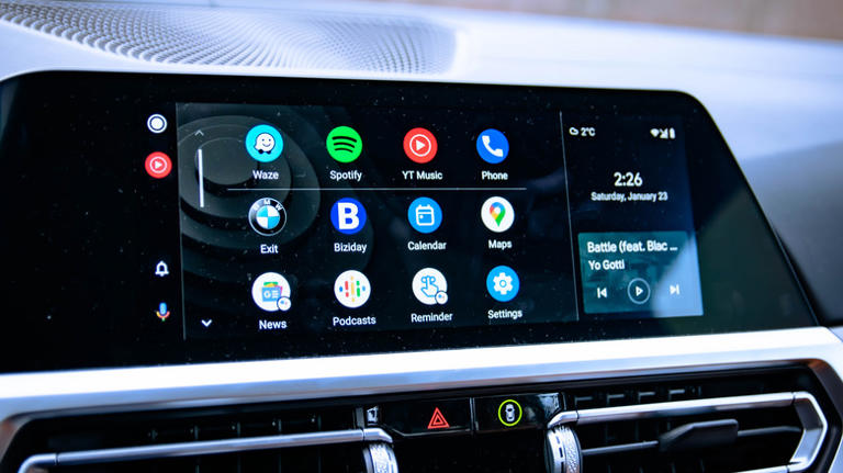 A vehicle's infotainment screen displaying several apps and a music player within Android Auto