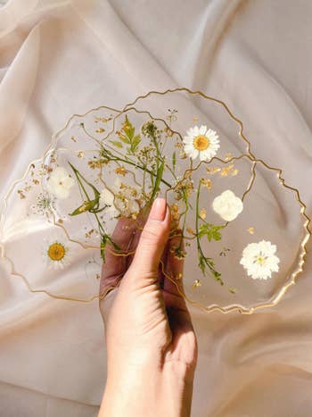 Set of transparent coasters with uneven edged gold rim and white pressed flowers inside
